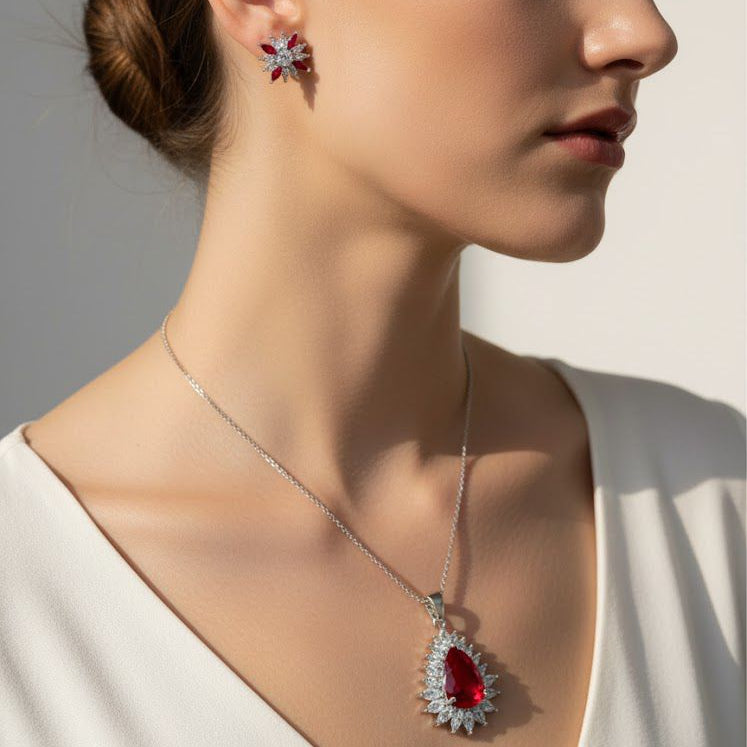 Woman wearing a necklace and earrings with a red gemstone on a neutral background