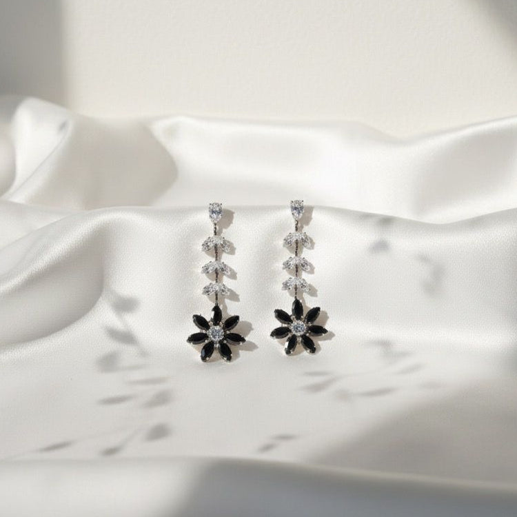 Pair of silver earrings with black stones on a white satin background