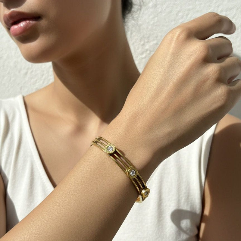 Woman wearing a gold bracelet with small stones on a plain background