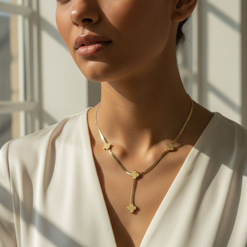 Woman wearing a gold necklace with a white top in a softly lit room.