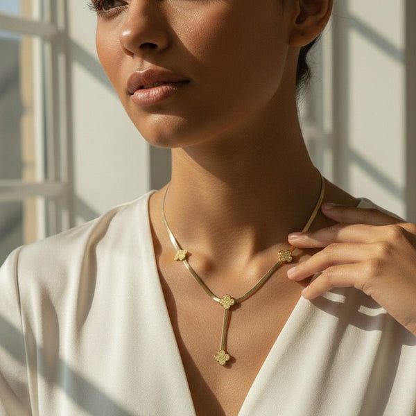 Woman wearing a gold necklace with a white top, sunlight filtering through.