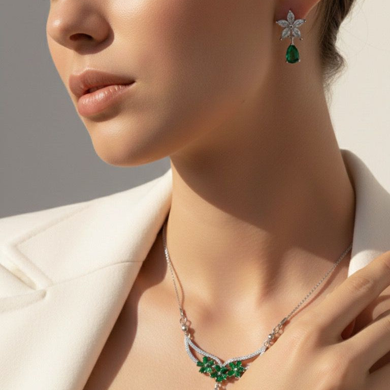 Woman wearing a necklace and earrings with green gemstones against a neutral background