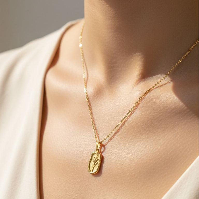 Gold necklace with a pendant on a person wearing a white top.
