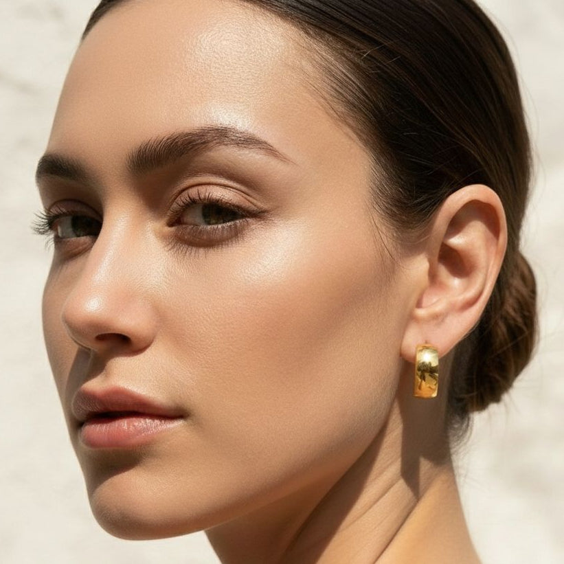 Close-up of a woman wearing gold earrings with a neutral background
