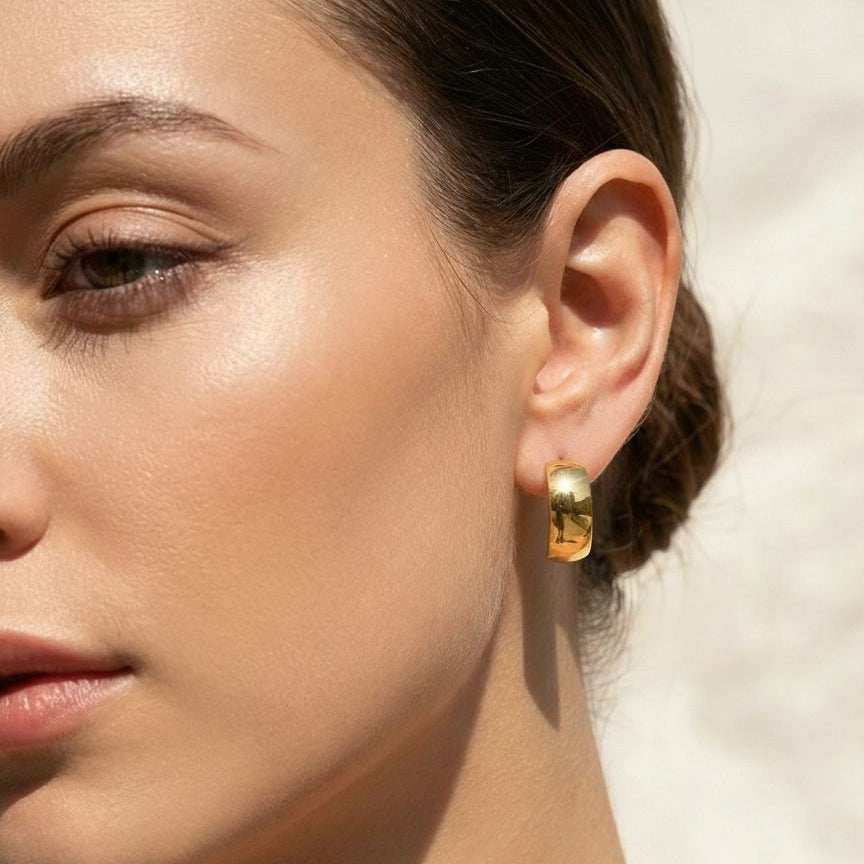 Close-up of a woman wearing gold hoop earrings with a neutral background