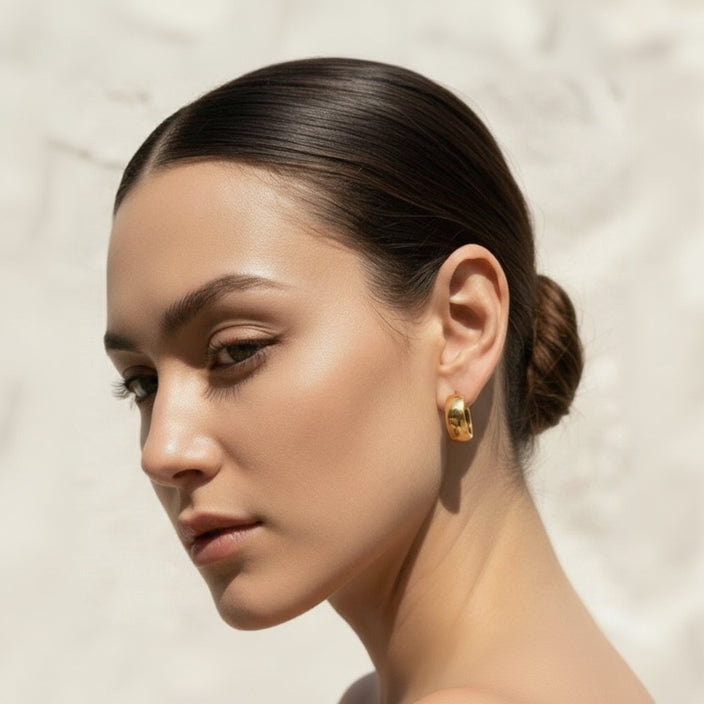 Woman wearing gold earrings against a neutral background