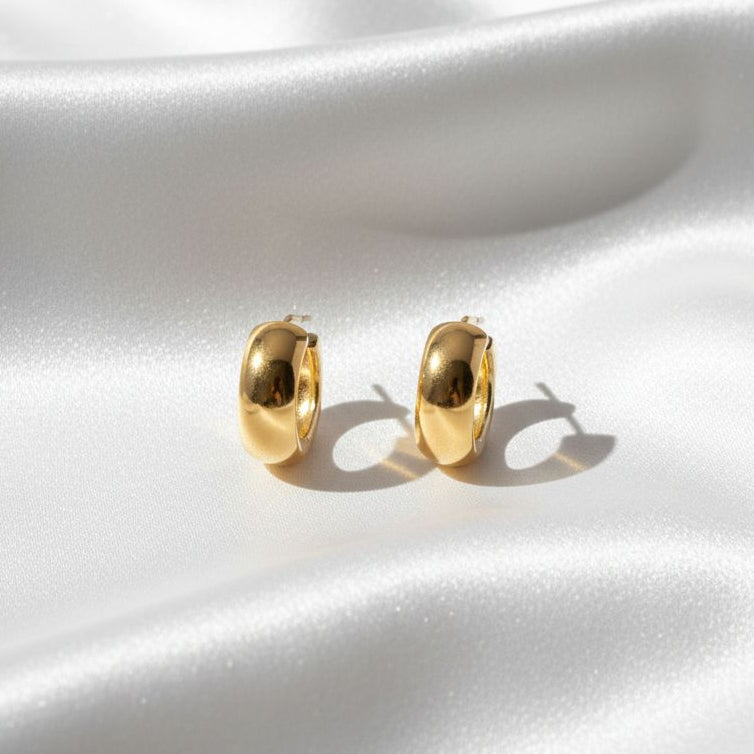 Gold hoop earrings on a white satin surface