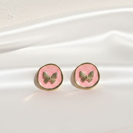 Pink butterfly earrings on a white fabric background