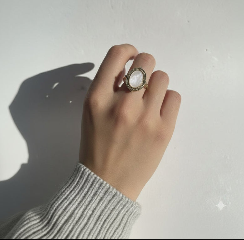 Hand wearing a gold ring with a large gemstone on a plain background