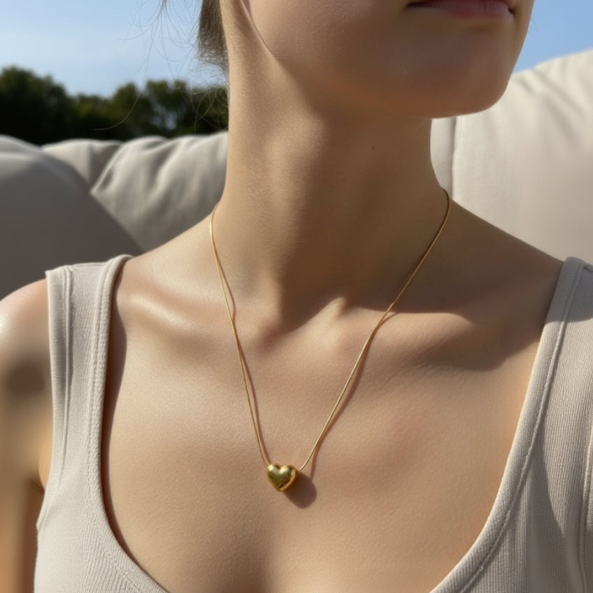 Gold necklace with a heart pendant on a person wearing a light-colored top.