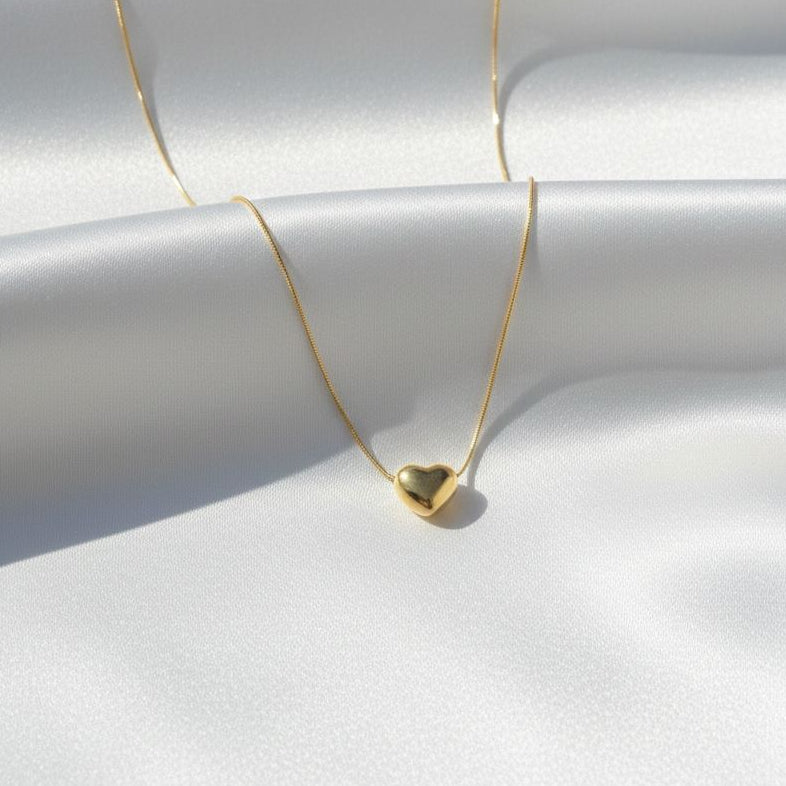 Gold necklace with a heart pendant on a white fabric background