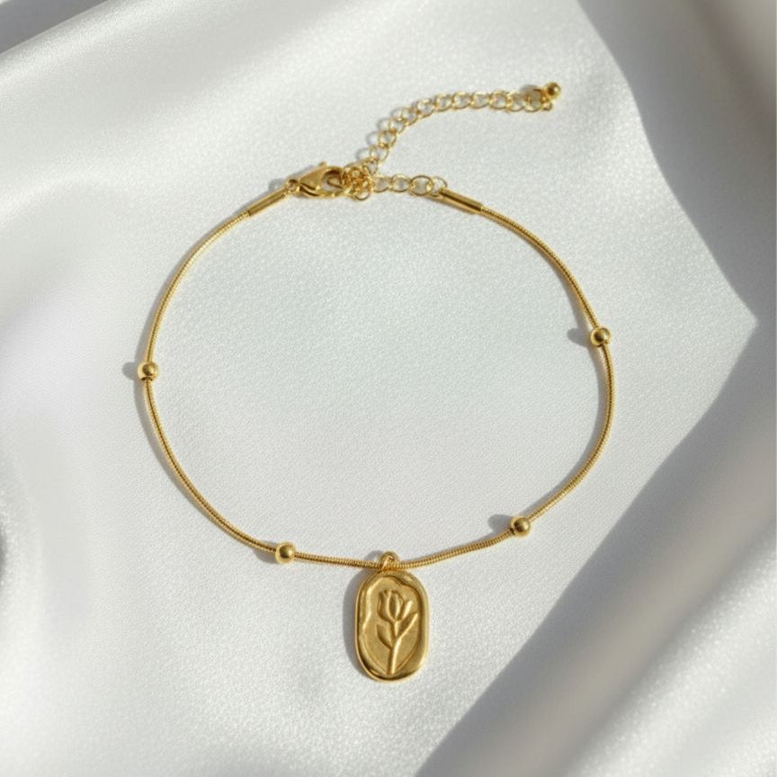 Gold bracelet with a floral charm on a white satin background