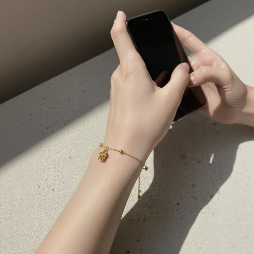 Hand holding a smartphone with a gold bracelet on a light surface
