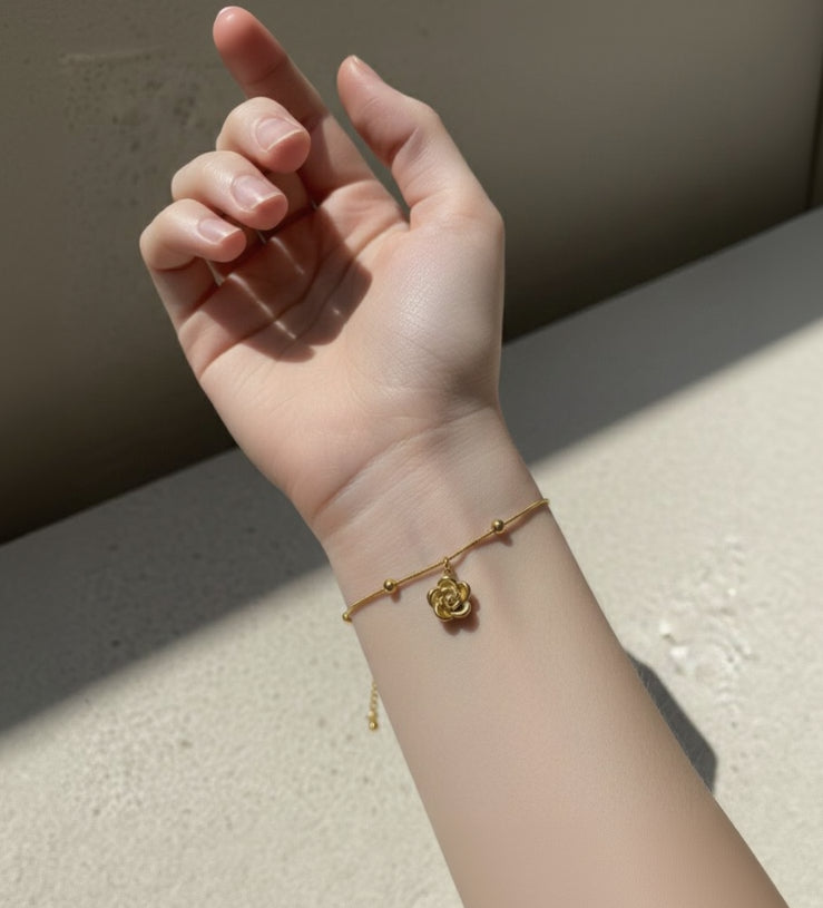 Hand wearing a gold bracelet with a rose design on a neutral background