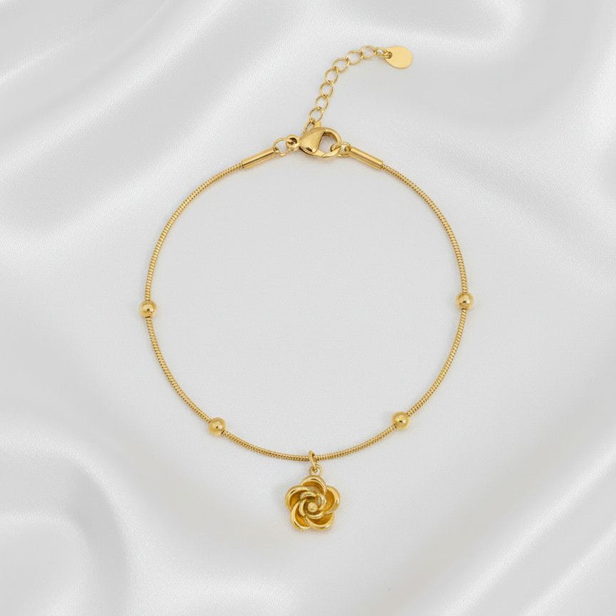 Gold bracelet with a floral charm on a white fabric background