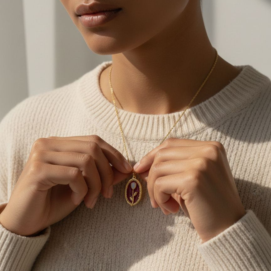 Person wearing a beige sweater holding a gold necklace with a pendant.