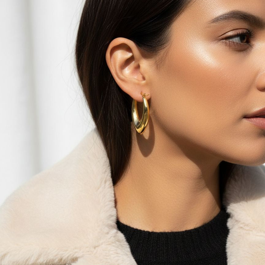 Close-up of a person wearing gold hoop earrings with a blurred background