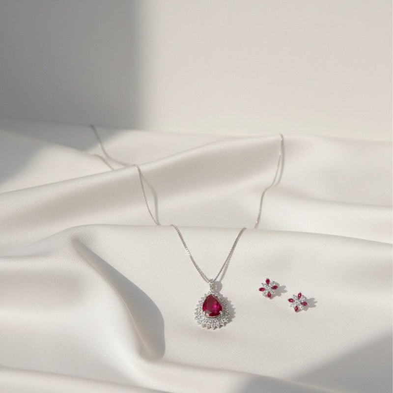 Silver jewelry set with a red gemstone on a white fabric background